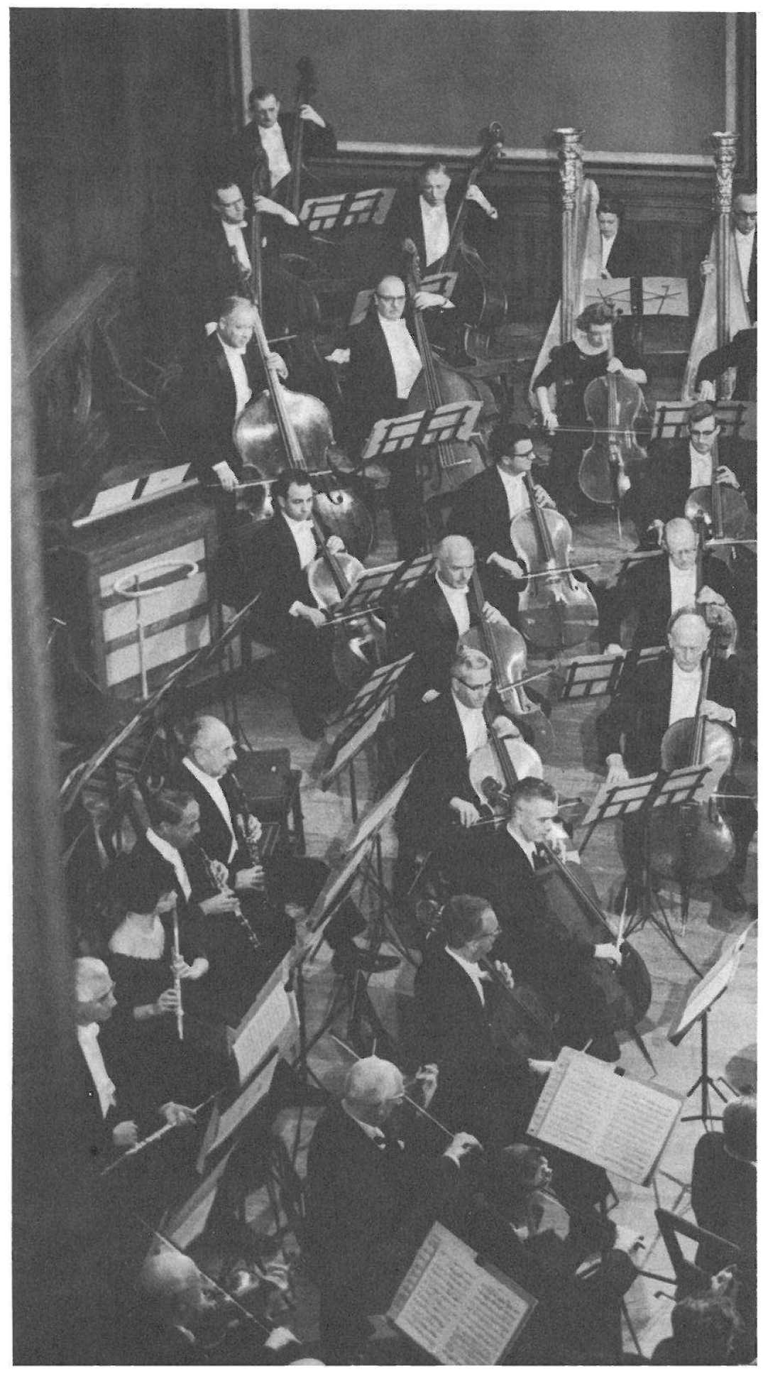 Photograph (no printed caption): the orchestra seen from above — double basses and harps at the back, cellos, and woodwind players in the foreground.